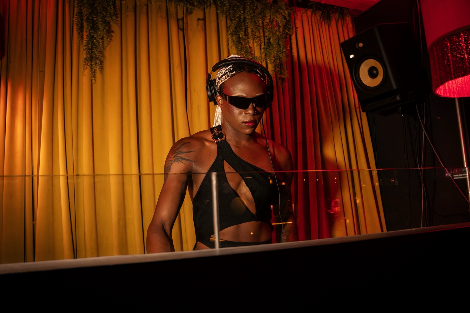 Mean Girl Machine in the DJ booth, amber light, headphones on